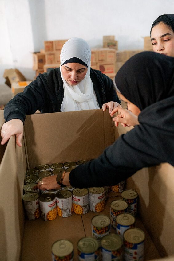Plan staff loading a box filled with canned food for Gaza.